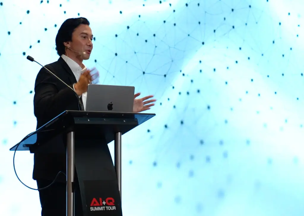 Velco Dar speaking at a lectern at the AI+Q Summit Tour