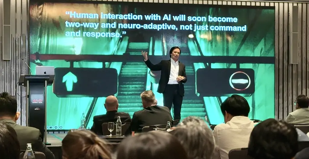 Velco Dar on stage at the AI+Q Summit Tour, with a slide reading Human interaction with AI will soon become two-way and neuro-adaptive
